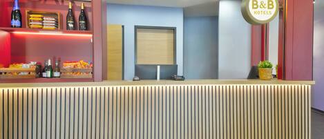 Un mostrador de recepción de hotel con diseño de paneles de madera, un letrero que dice 'BAR' y un letrero de 'B&B HOTELS'.