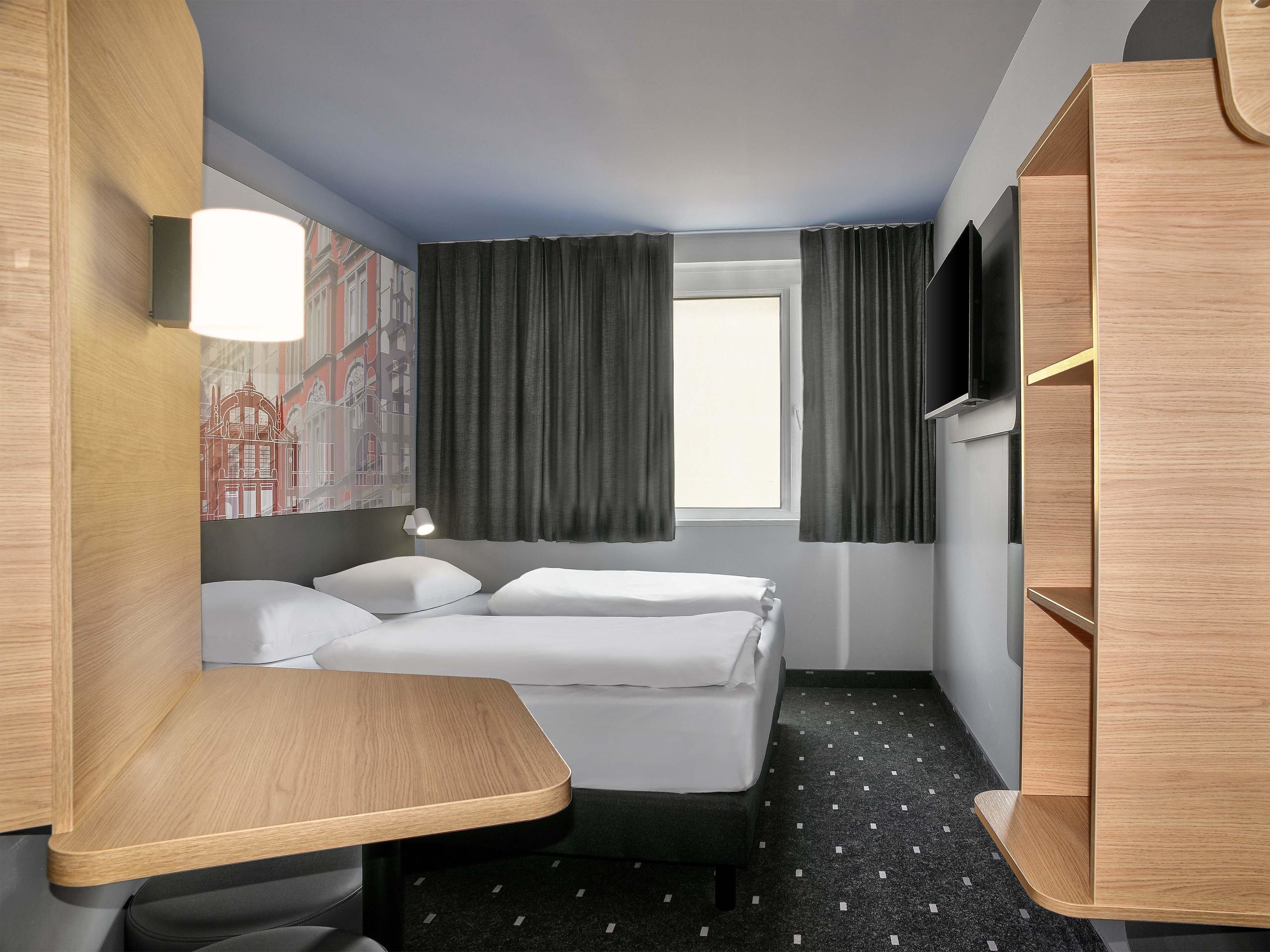 A hotel room with a bed, a desk, a TV, and a window with curtains.
