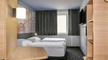 A hotel room with a bed, a desk, a TV, and a window with curtains.