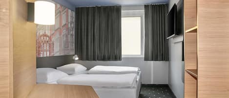 A hotel room with a bed, a desk, a TV, and a window with curtains.