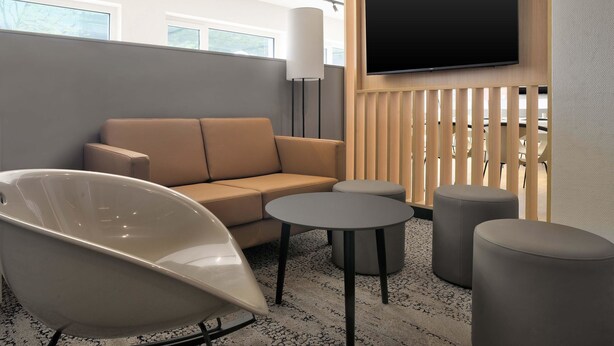 Un espace détente moderne avec un canapé, un fauteuil blanc et des tables rondes.