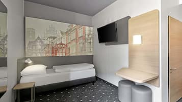 A modern hotel room with a bed, a small bedside table, a mounted TV, and a large window with a cityscape view.