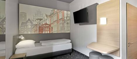 A modern hotel room with a bed, a small bedside table, a mounted TV, and a large window with a cityscape view.
