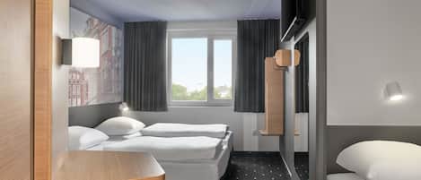 Habitación de hotel con dos camas, una mesita, una silla, una ventana con cortinas y un televisor montado en la pared.
