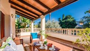 A covered patio with a wooden table set for dining, a sofa with cushions, and a potted plant. - House in Alcudia Can Jaume with swimming pool (Alcúdia)