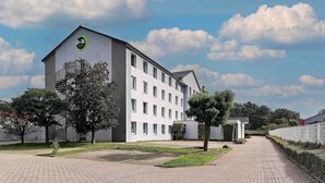 A modern hotel building with a prominent B&B logo, a covered outdoor area, and a paved walkway. - B&B Hotel Köln-Airport (Cologne)