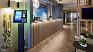 A modern reception desk with a digital check-in kiosk, a reception area, and a view into the hotel's interior. - B&B Hotel Köln-Airport (Cologne)
