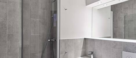 Un baño moderno con ducha de vidrio, lavamanos blanco y un espejo grande.