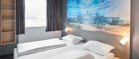 A hotel room with a large bed, a bedside table, a built-in shelf, and a window with curtains.