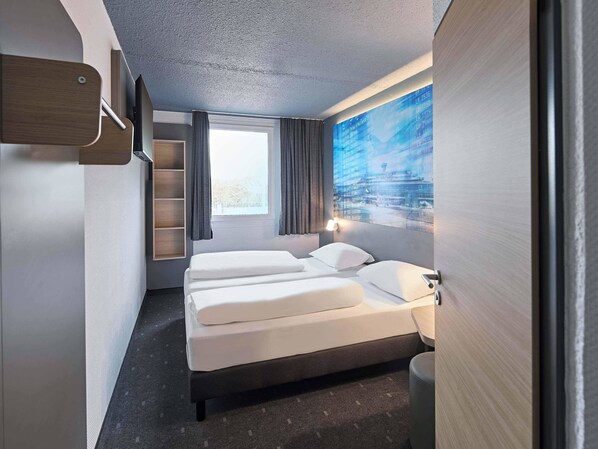 A hotel room with a bed, a desk, a chair, a window, and a wall-mounted TV. - B&B Hotel Köln-Airport (Cologne)