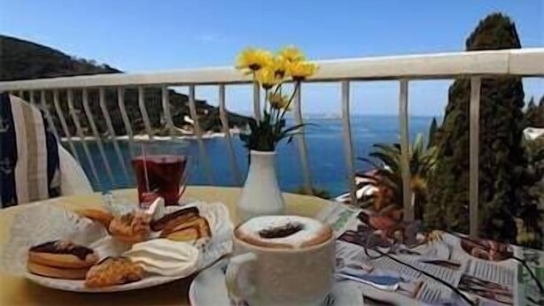 A table with pastries, a drink, and a vase with yellow flowers, overlooking a coastal view. - Kompas (Balchik)