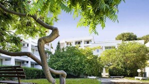 A tree-lined pathway leading to a building with multiple balconies. - Kompas (Balchik)