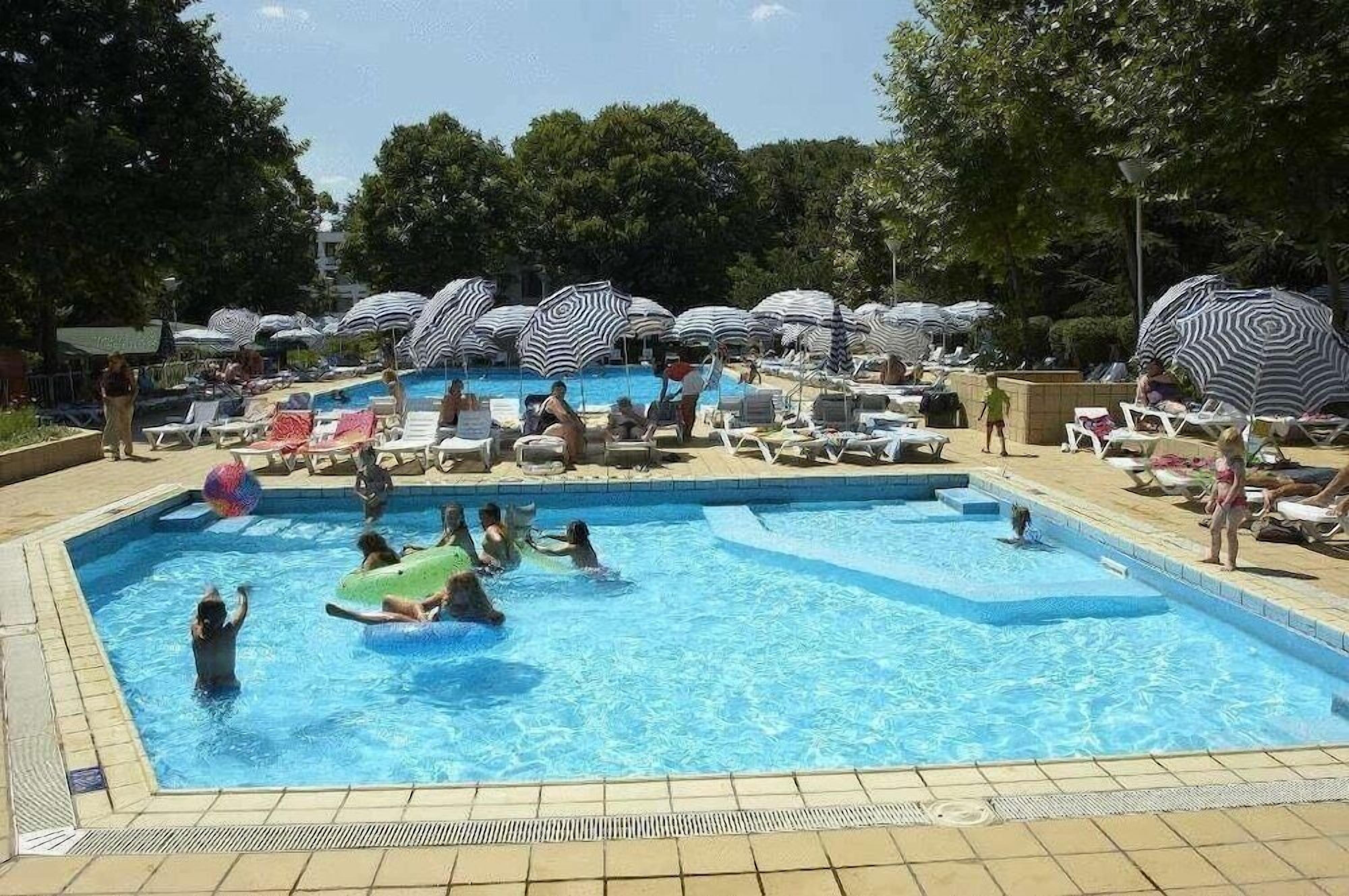 A swimming pool area with multiple lounge chairs and umbrellas.