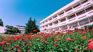 A multi-story building with balconies, surrounded by a garden with various flowers. - Kompas (Balchik)