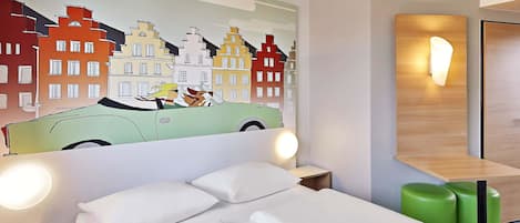 A hotel room with a bed, green ottoman, and a wall mural of a car and buildings.