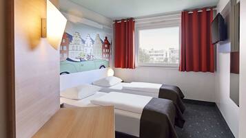 Een hotelkamer met twee bedden, een klein tafeltje, een tv aan de muur en een raam met rode gordijnen.