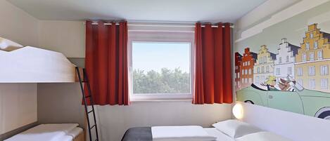 Quarto de hotel com beliches, janela com cortinas vermelhas, luminária e um mural com vista para a cidade.
