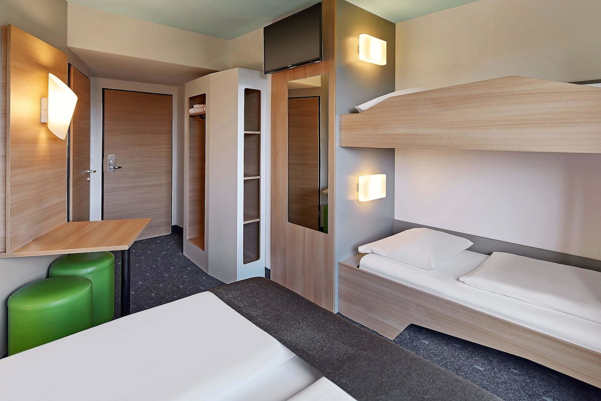 Une chambre d’hôtel moderne équipée d’un lit superposé, d’un bureau et d’une armoire.