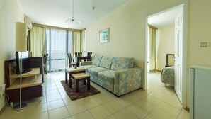 Una sala de estar con un sofá, un televisor, una mesa de comedor con sillas y una mesita de noche con lámpara.