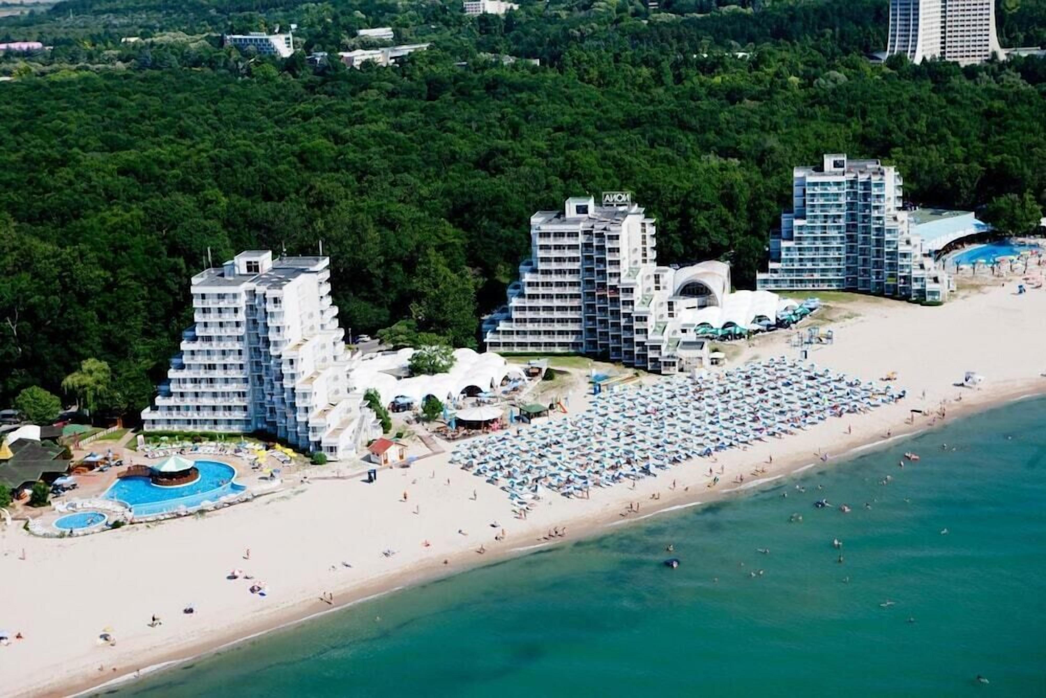 A coastal hotel with multiple high-rise buildings, a large sandy beach, and a pool area.