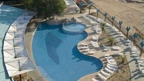 Un resort con una gran piscina, sillas de descanso y una playa al fondo.