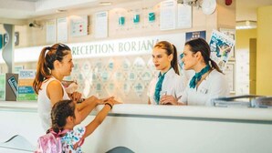 Un área de recepción con mostrador, un letrero que dice "RECEPTION BORJANA" y un niño extendiendo la mano hacia un miembro del personal.