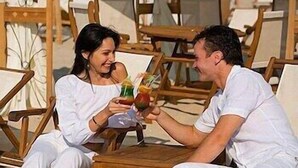 Dos personas sentadas en una mesa de madera al aire libre, sosteniendo bebidas.