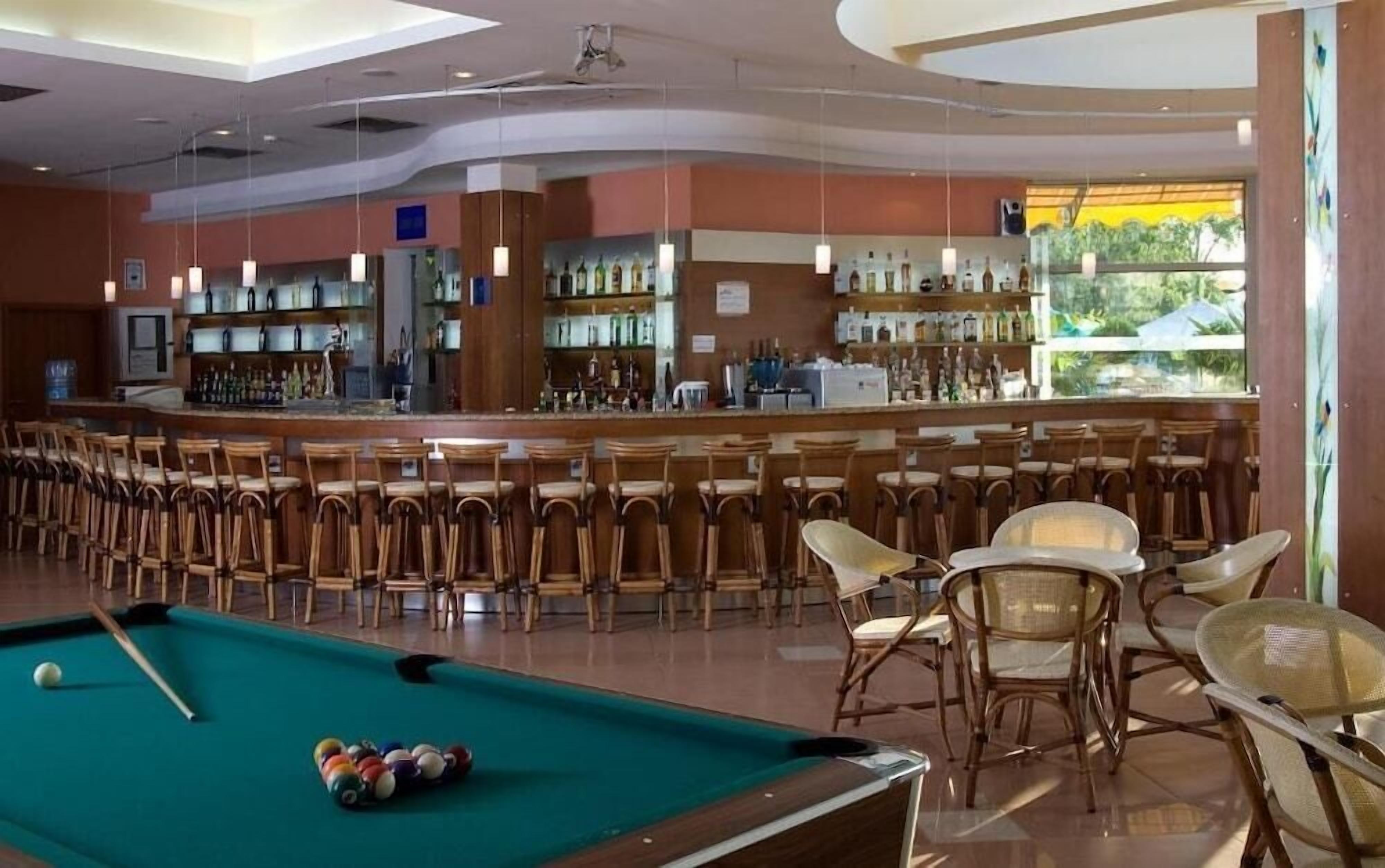 A bar area with a pool table, bar stools, and a bar stocked with bottles.