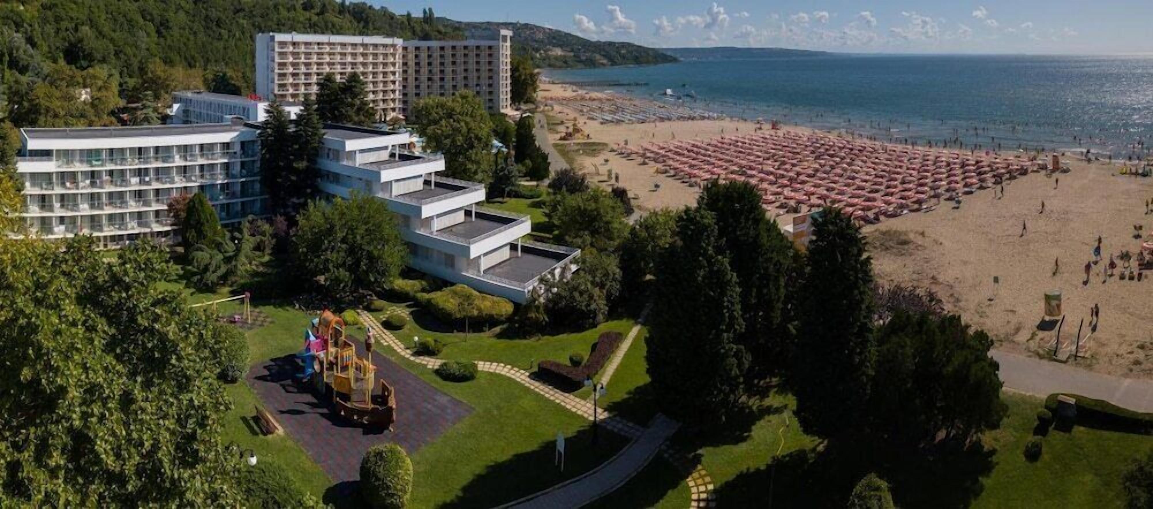 Un hotel de varios pisos, una playa con numerosos paraguas y un parque infantil.