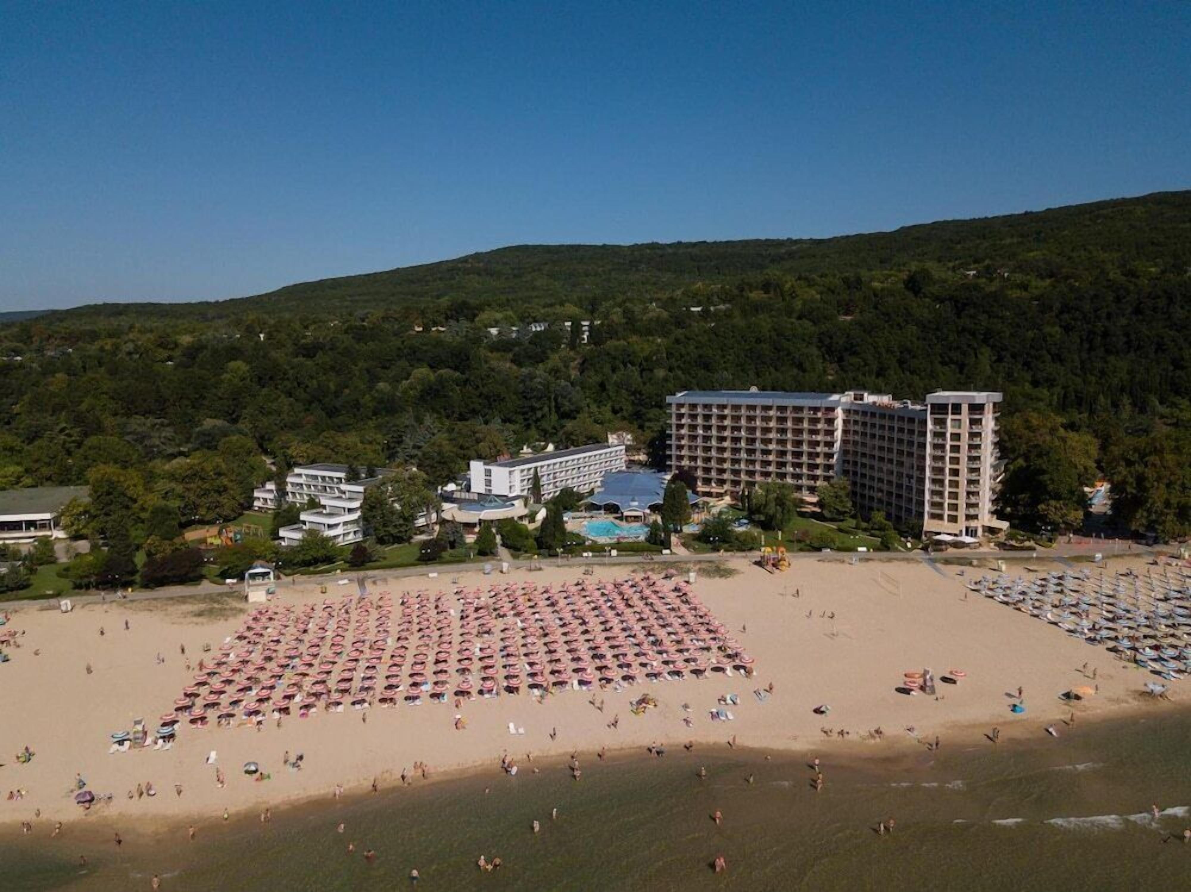 A beach with rows of pink umbrellas and a large hotel complex in the background.