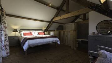 Una camera da letto con pavimento in legno, un letto con biancheria rossa e bianca, un comodino, una cassettiera e uno specchio appeso al muro.