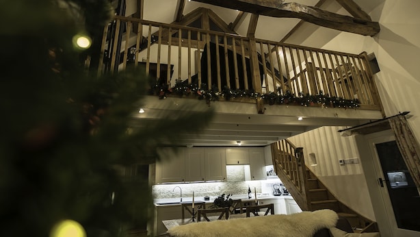 Ein geräumiges Loft mit hoher Decke, freiliegenden Holzbalken, einer Küchenzeile und einer Treppe, die in eine obere Ebene führt.