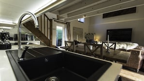 Eine moderne Küche mit einem großen Spülbecken, einer Holztreppe und einer gemütlichen Wohnbereits mit Sofa und Flachbildfernseher.