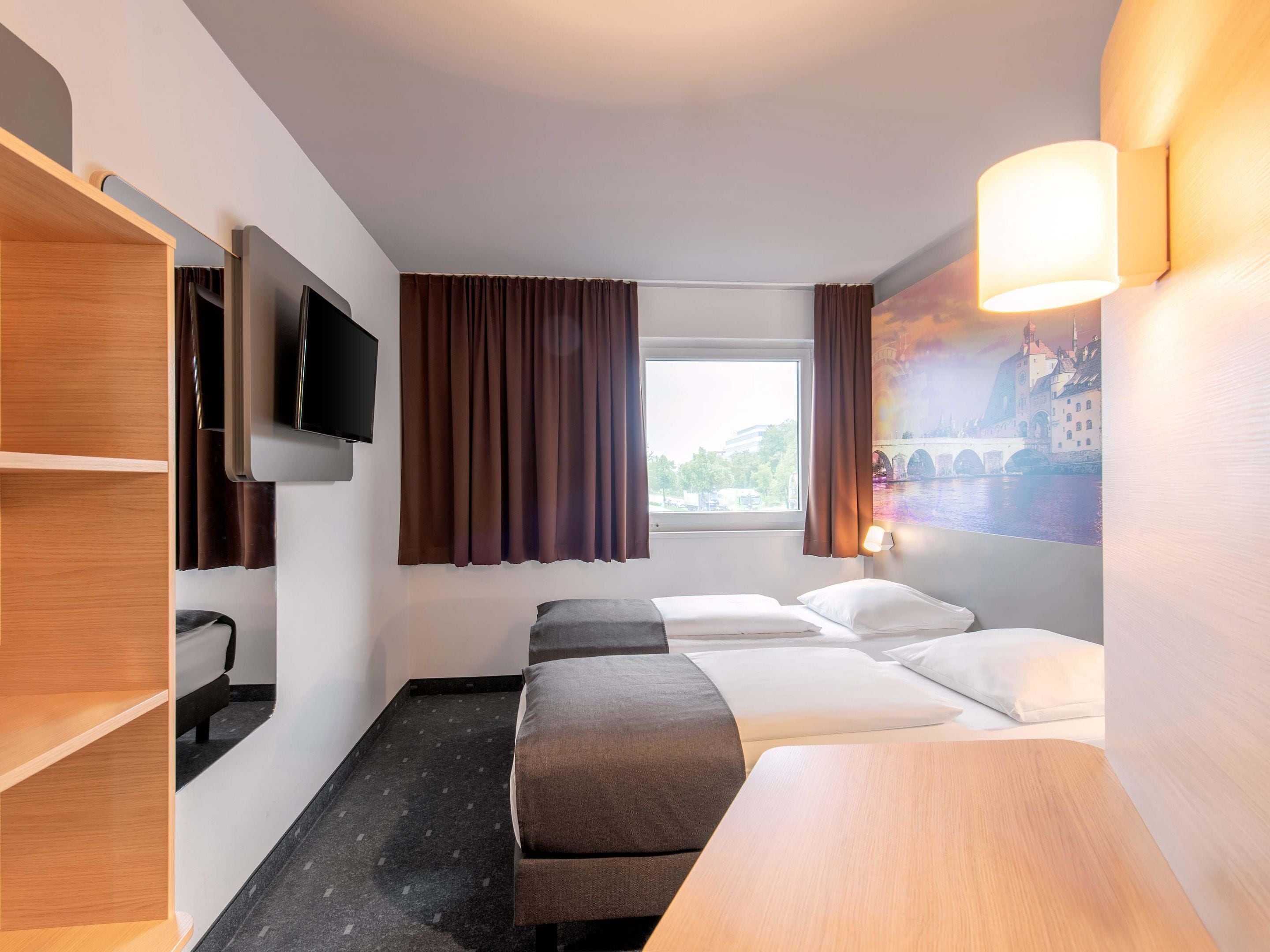 Een hotelkamer met een bed, een bankje, een televisie, een raam met gordijnen en een wandlamp.