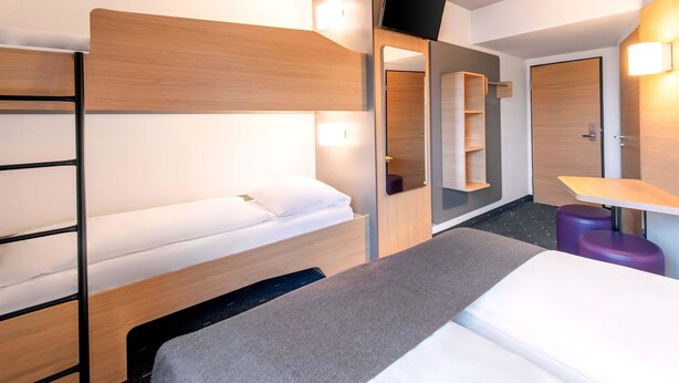 Una habitación de hotel moderna con literas, un escritorio, un espejo y una televisión.