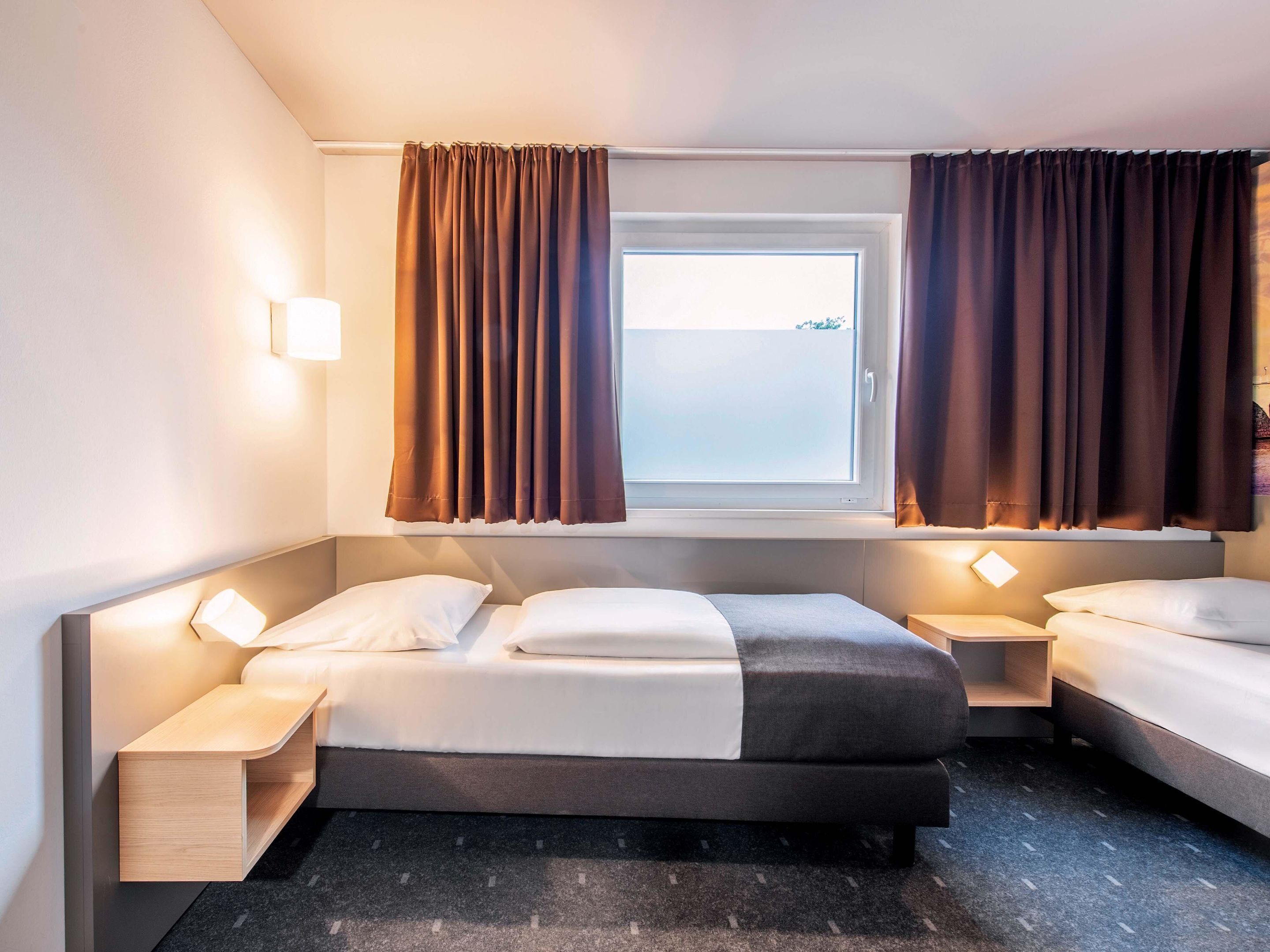 Une chambre d’hôtel avec un grand lit, deux tables de chevet, une fenêtre avec des rideaux et une vue sur l’extérieur.