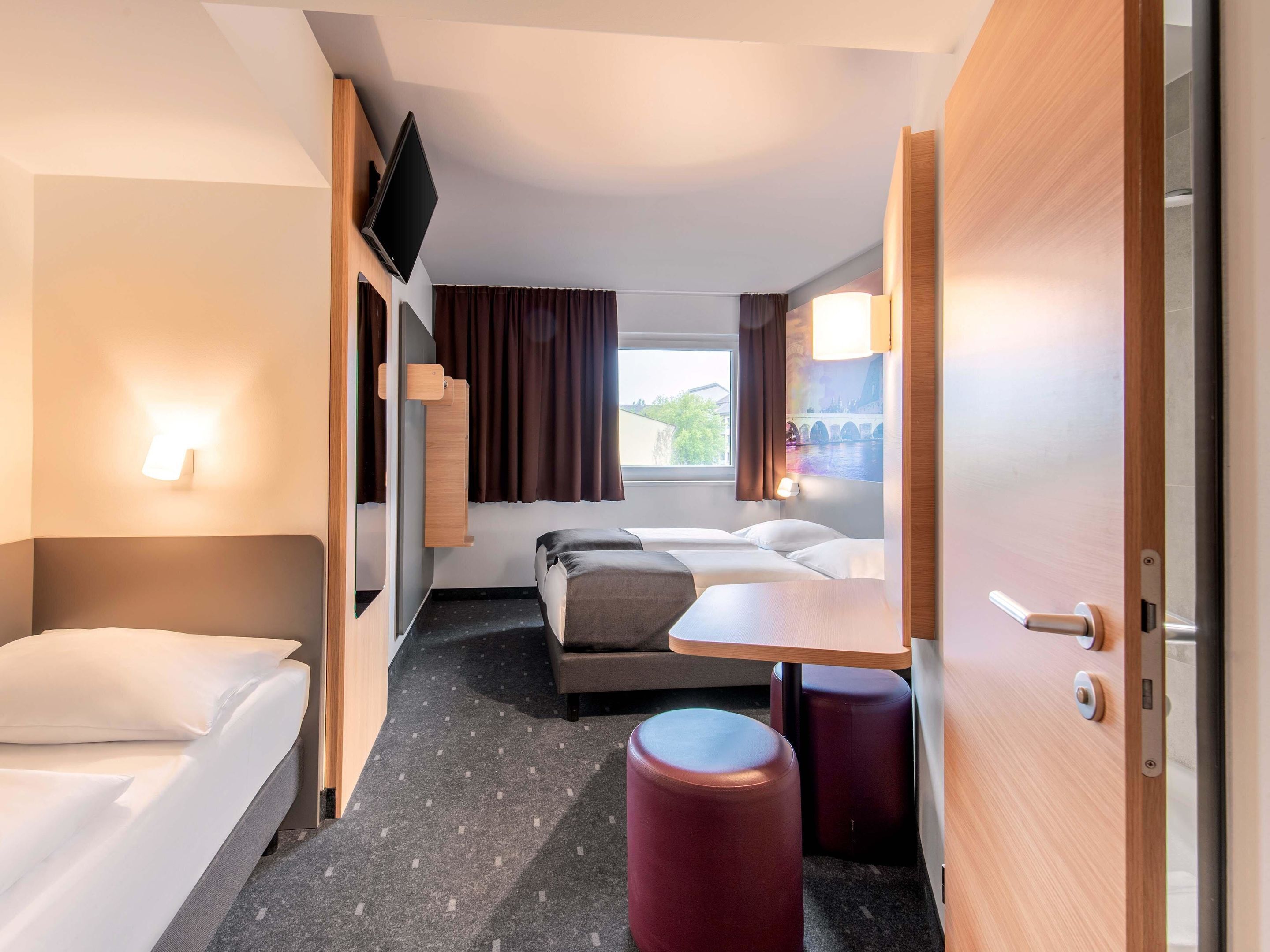 A compact hotel room with a bed, a sofa, a small table, and a TV mounted on the wall.