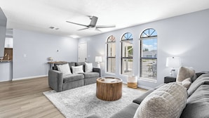 A modern living room with a grey sofa, a round coffee table, and a ceiling fan. - Luxury Living & Heated Pool Near Anna Maria Island (Bradenton)