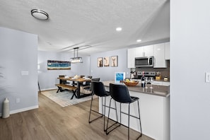 A modern kitchen with white cabinets, a microwave, and a dining area with a wooden table and black chairs.