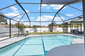 A swimming pool with a covered area, lounge chairs, and a view of a residential neighborhood.