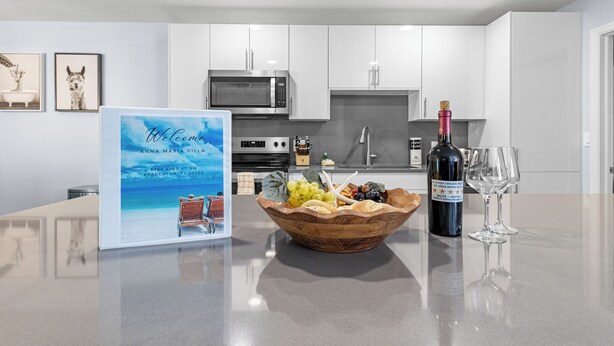 A kitchen with white cabinets, a microwave, a wine bottle, and a bowl of fruit on the counter. - Luxury Living & Heated Pool Near Anna Maria Island (Bradenton)
