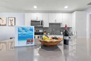 Una cocina con armarios blancos, un microondas, una botella de vino y un bol de fruta sobre la encimera.