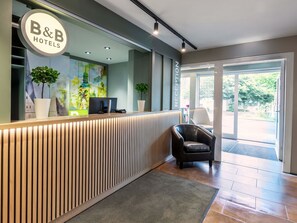 A reception desk with a B&B Hotels sign, a computer, and a potted plant.
