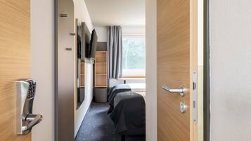Una habitación de hotel con cama, televisión, escritorio y ventana con cortinas.