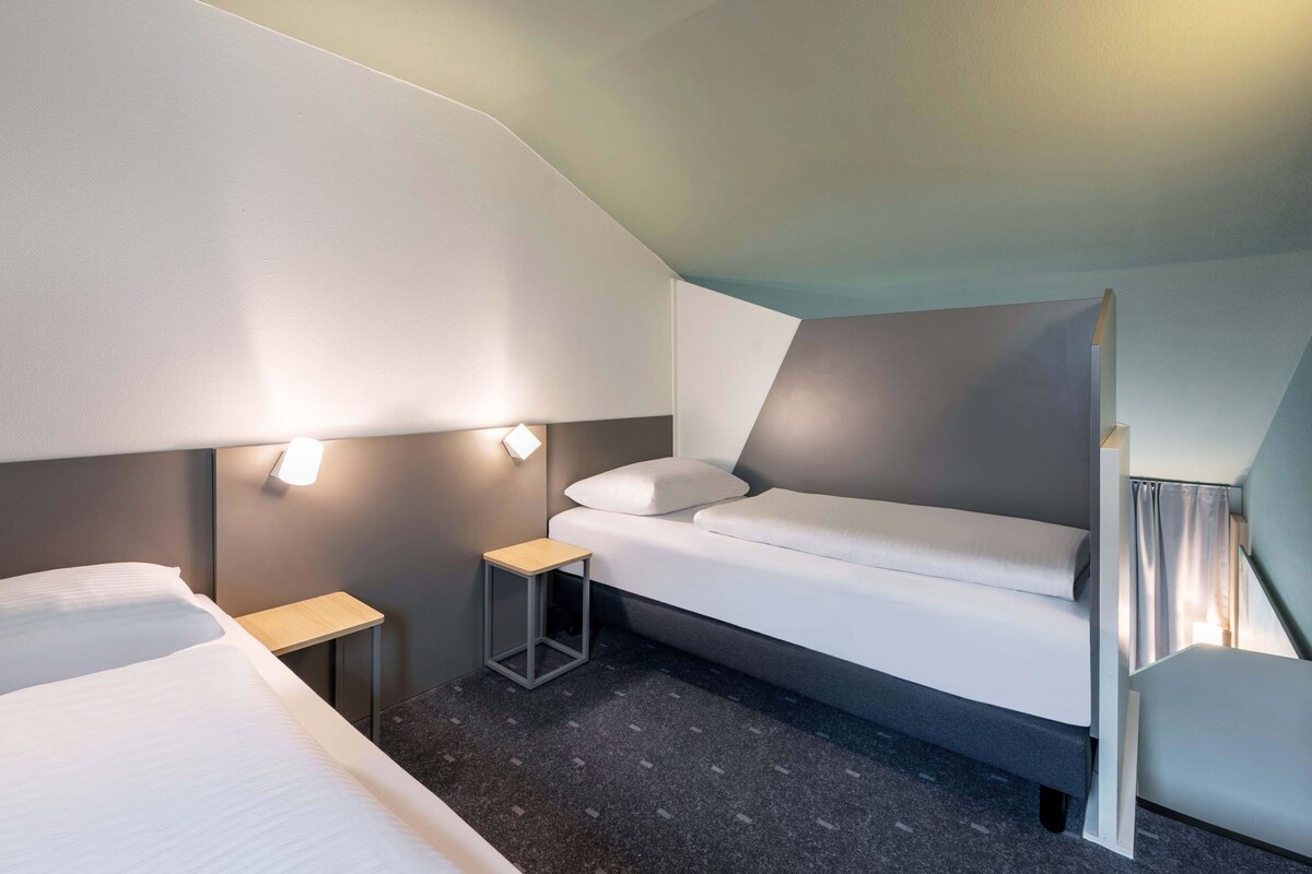 A modern hotel room with a bunk bed, a small bedside table, and a wall-mounted light fixture.