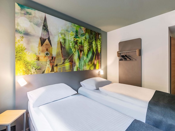 A hotel room with a bed, a nightstand, a wall-mounted coat rack, and a large cityscape painting.