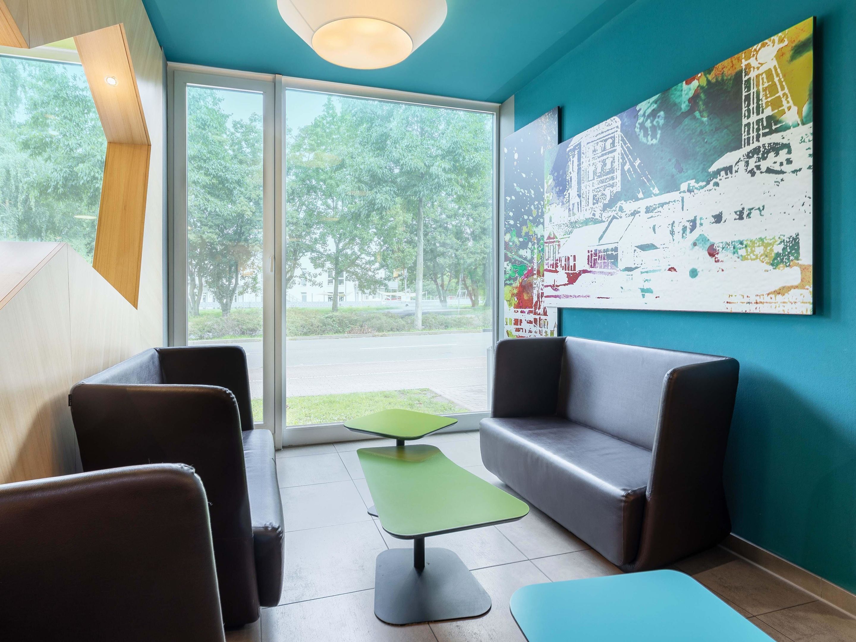 A modern waiting area with leather sofas, a green table, and a large window offering a view of the outdoors.