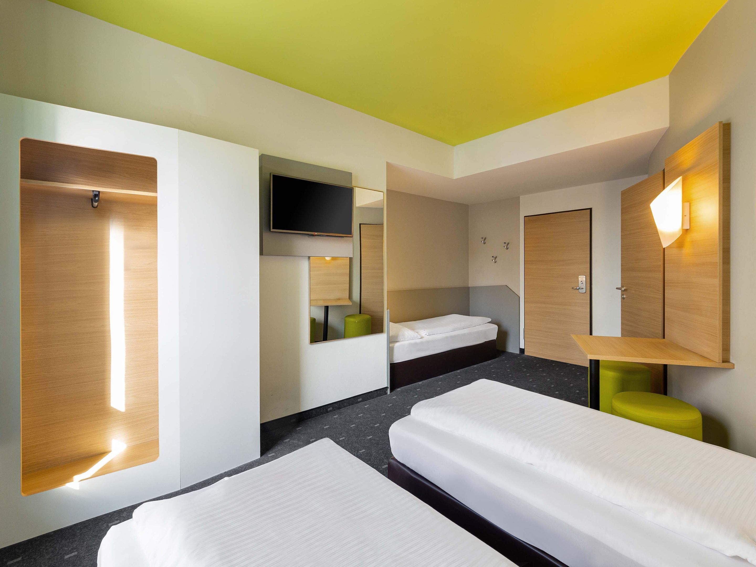 A hotel room with two single beds, a TV mounted on the wall, and a mirror above the bed.