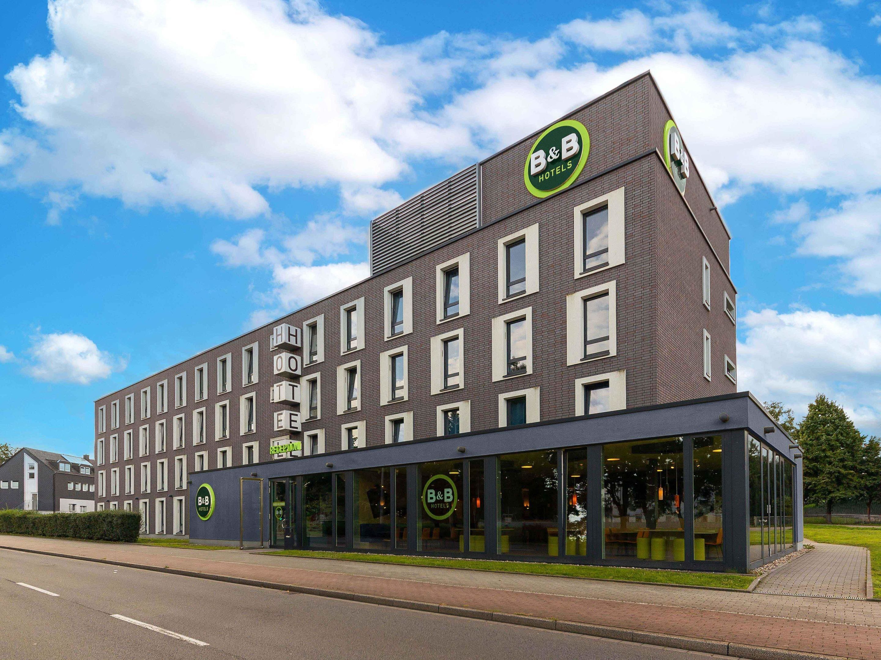 A B&B hotel with a modern design, featuring a reception area and multiple rooms visible through large windows.