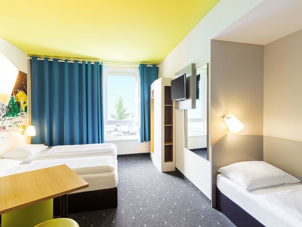 A hotel room with a bed, a desk, a chair, a TV, and a window with curtains.